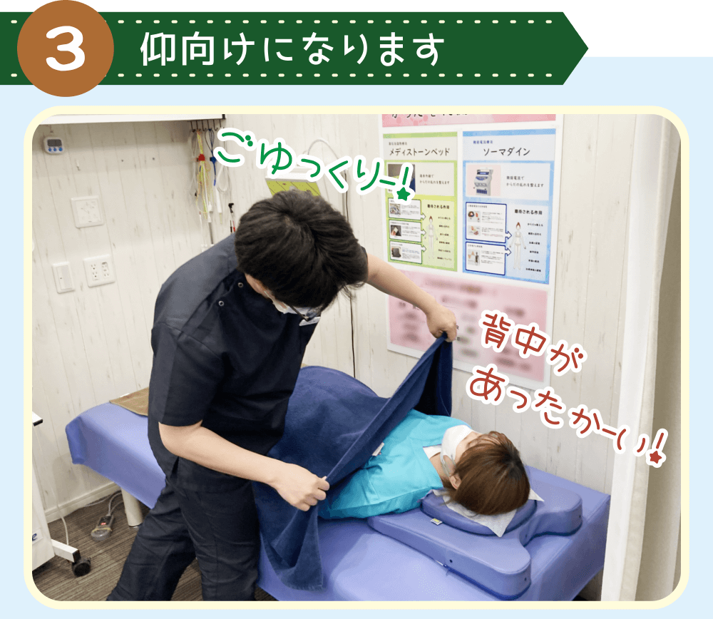 施術準備中、メディストーンベッドに仰向けで横になる佐藤に、長尾がタオルをかけている様子