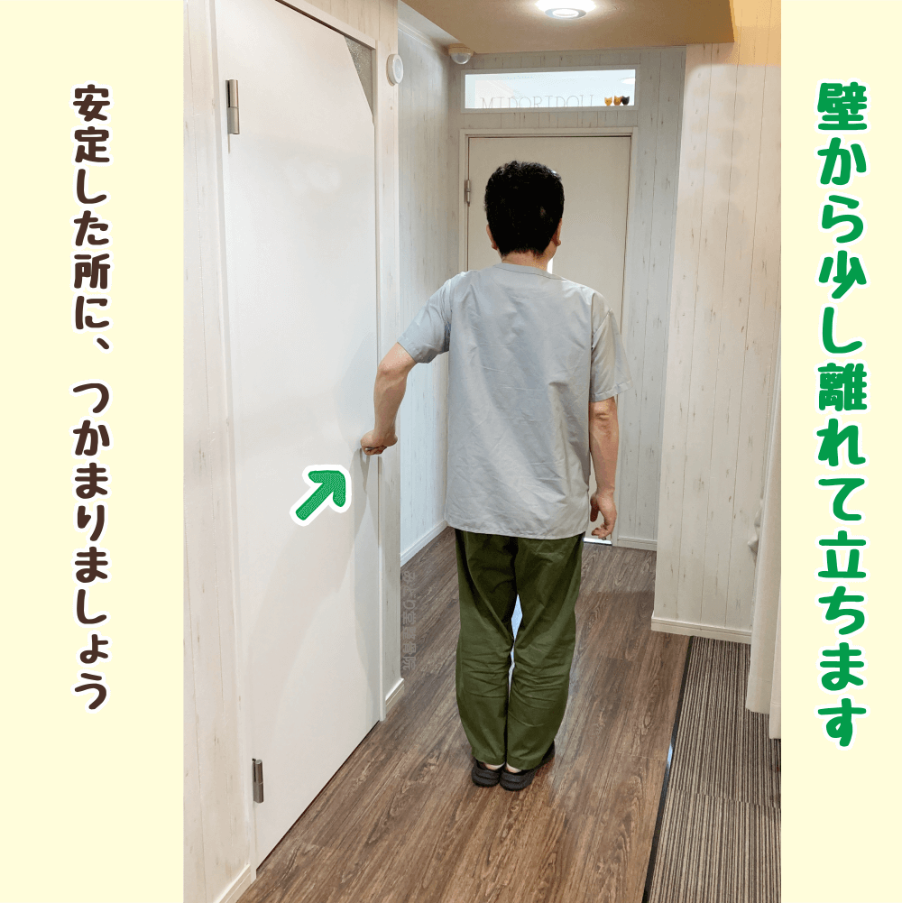 壁から少し離れて立ち、左手を安定した場所に添えるウォームアップの開始ポジション。体を伸ばす準備動作。